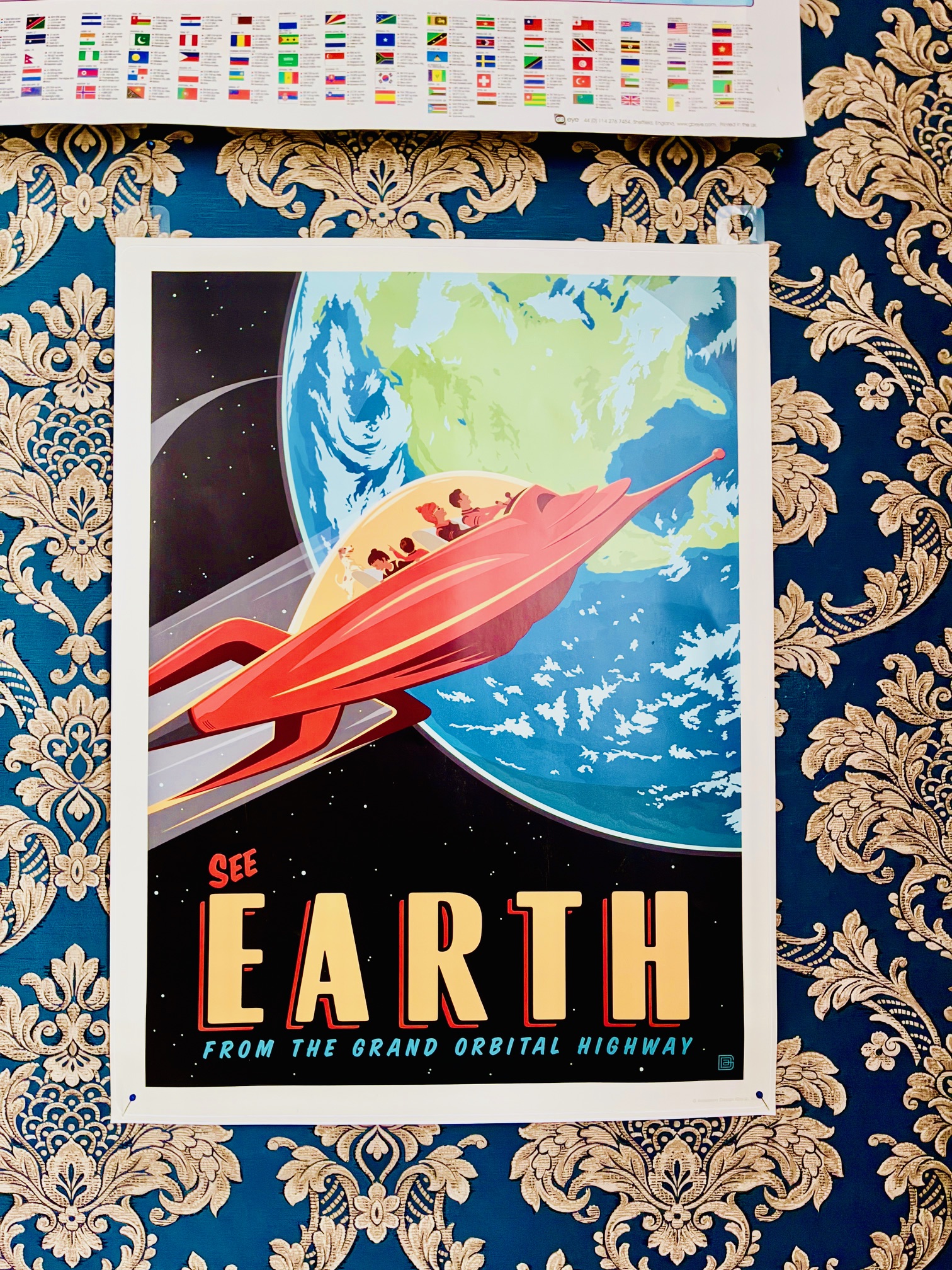 Buntes Poster im Retro-Stil vor einer blau-goldenen, verschnörkelten Tapete. Poster zeigt Illustration eines roten Raumschiffs mit Passagieren vor der Erde im Weltraum mit dem Text 'SEE EARTH FROM THE GRAND ORBITAL HIGHWAY'