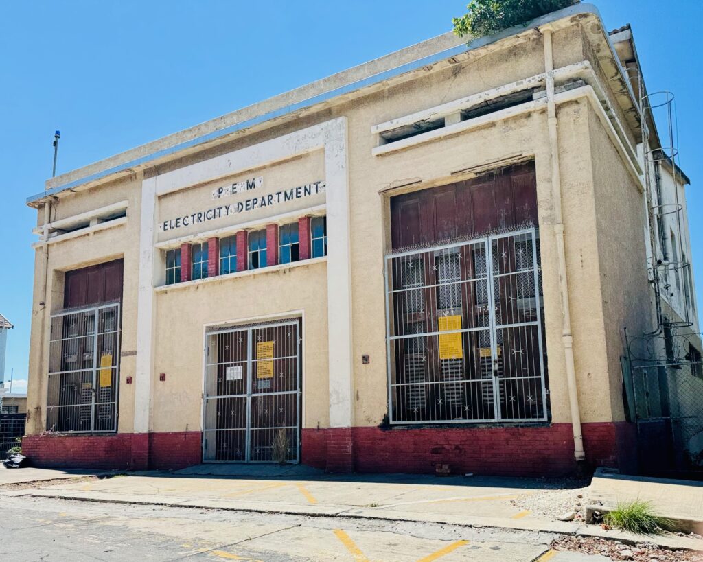 Fassade eines alten Gebäudes mit von Hand gemalter Aufschrift 'P.E.M. ELECTRICITY DEPARTMENT' und vergitterten Türen unter blauem Himmel