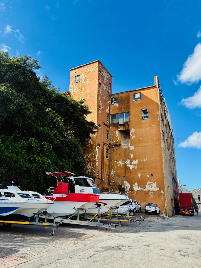 Mehrstöckiges, verwittertes Gebäude neben mehreren auf Anhängern abgestellten Booten unter blauem Himmel