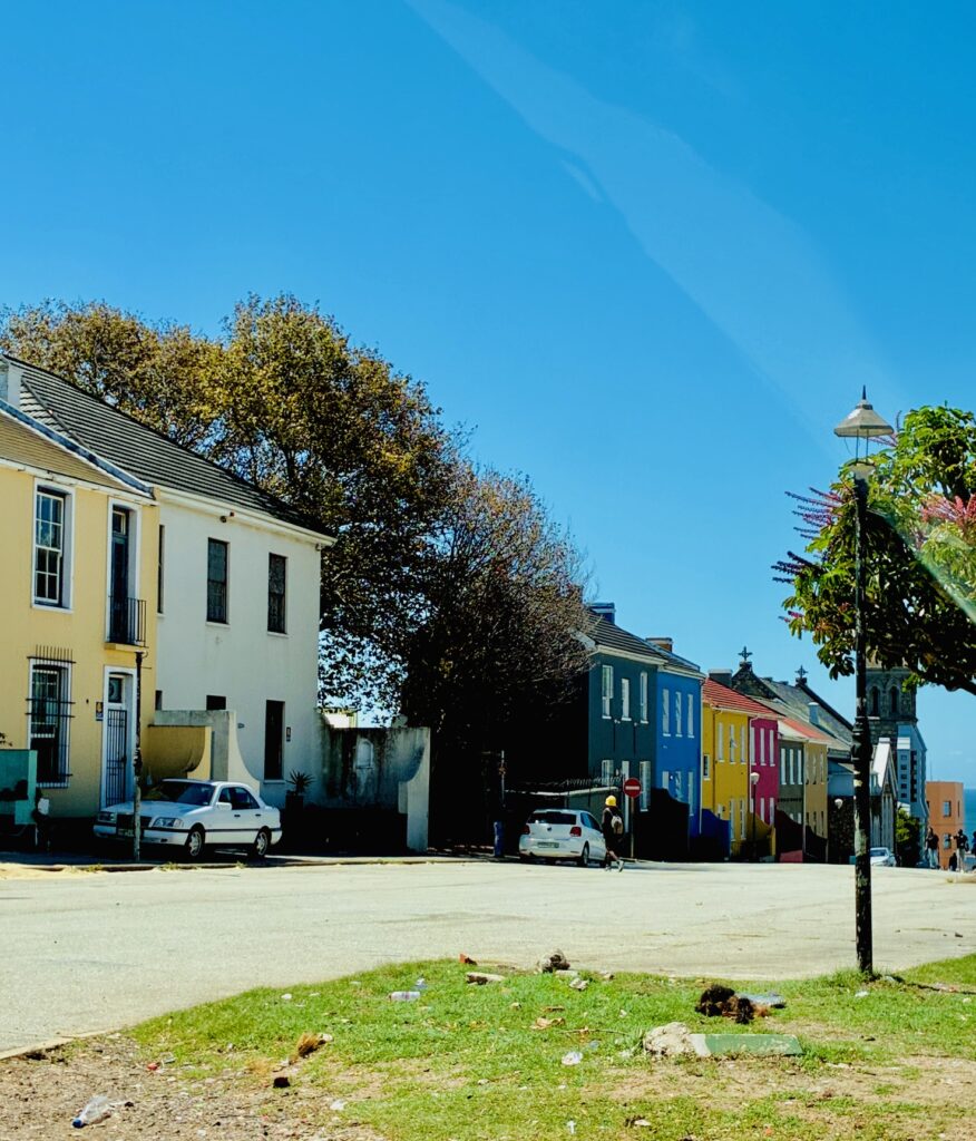 Straße mit zweistöckigen bunten Häusern und parkenden Autos unter blauem Himmel