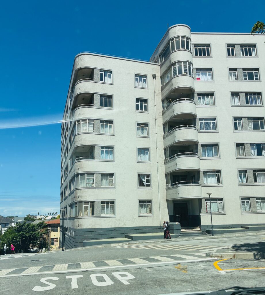 Mehrstöckiges Wohngebäude mit abgerundeten Balkonen an der Ecke und mehreren Fenstern an einer Straßenkreuzung unter strahlend blauem Himmel