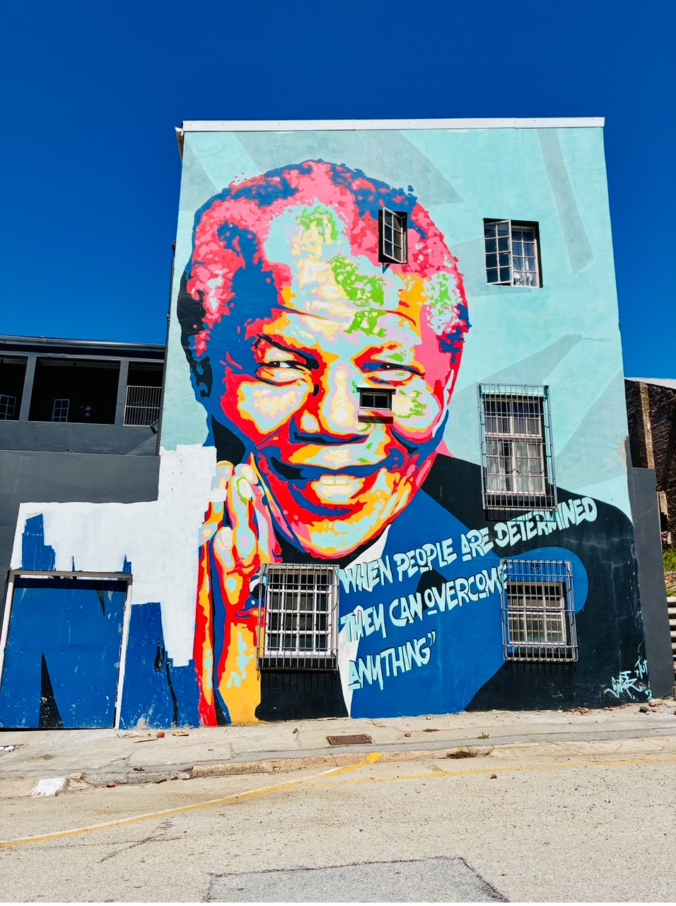 Großes Wandgemälde an einem Gebäude mit einem farbigen Porträt von Nelson Mandela und dem Schriftzug 'WHEN PEOPLE ARE DETERMINED THEY CAN OVERCOME ANYTHING'