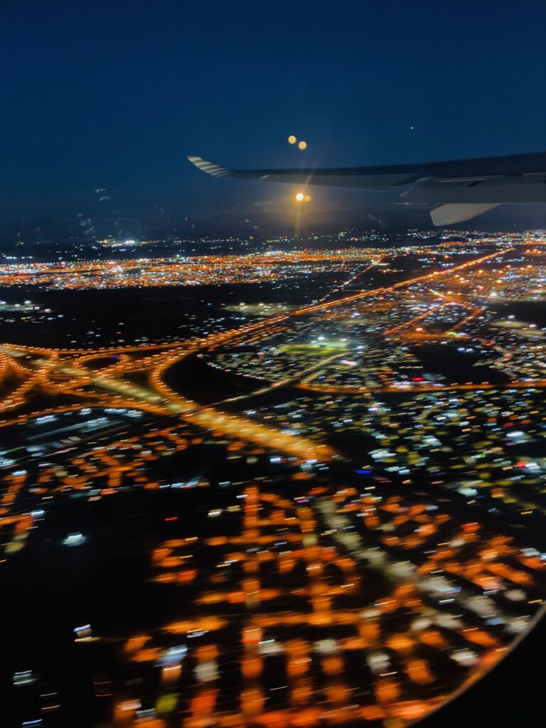 Blick aus einem Flugzeugfenster auf das nächtliche Kapstadt mit Straßen und Gebäuden sowie dem Flügel des Flugzeugs und dem orangefarbenen Mond