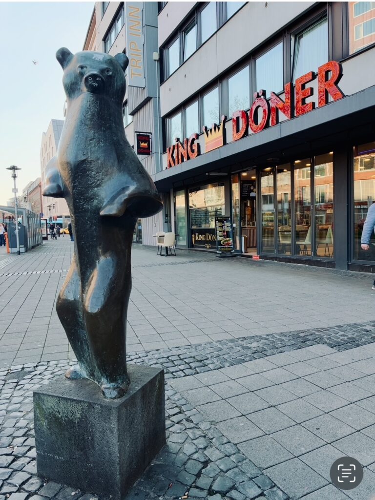 Bronzeskulptur eines aufrecht stehenden Bären auf einem quadratischen Sockel vor einem Gebäude mit dem Schriftzug 'KING DÖNER' in Münster