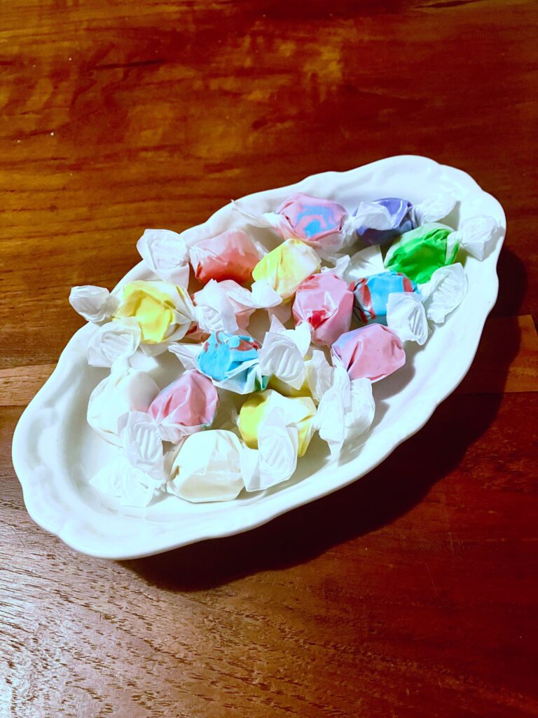 Weiße, ovale Porzellanschale mit bunten Bonbons auf einem Holztisch