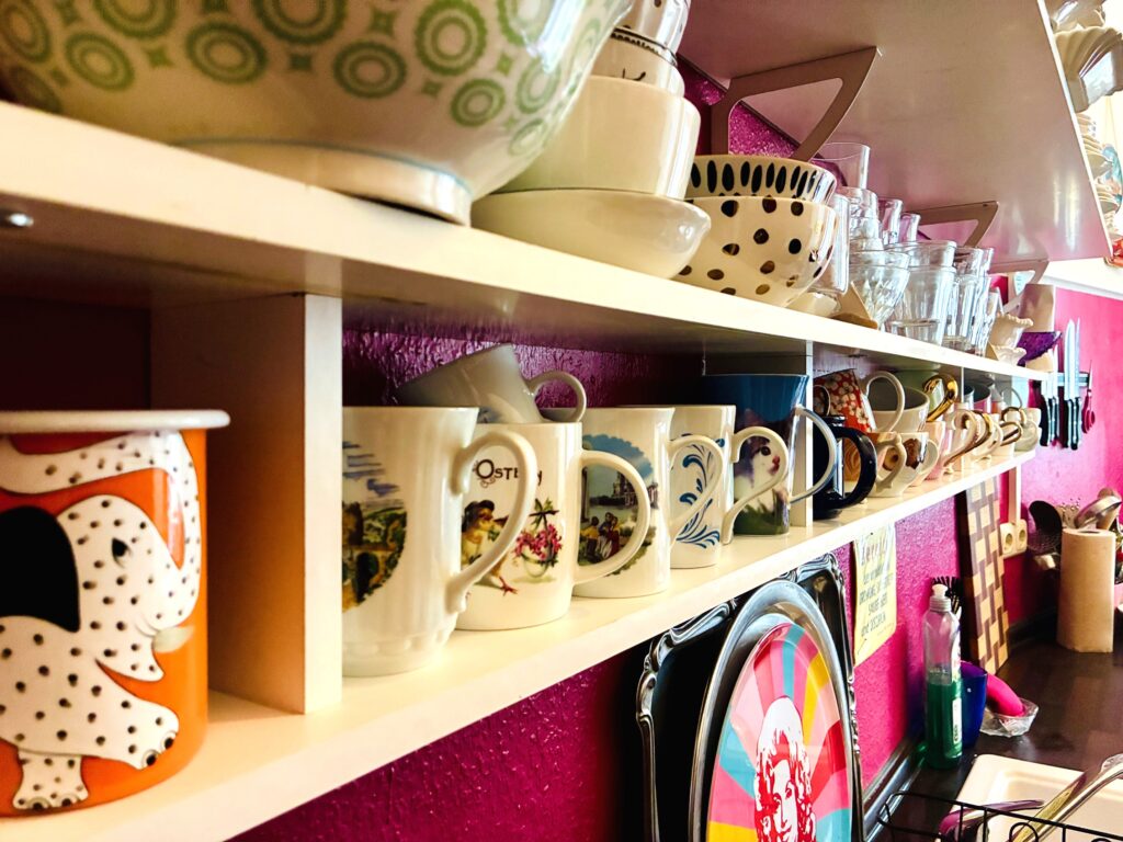 Regal mit einer Reihe verschiedener Kaffeetassen und Gläsern vor einer pinkfarbenen Wand