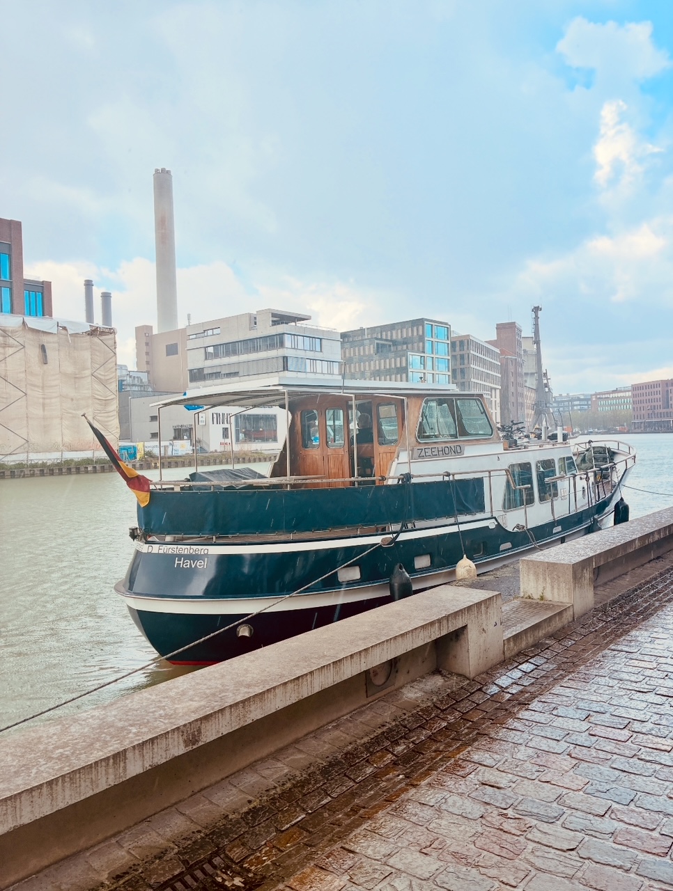 Motorboot mit dem Namen 'Zeehond' im Hafen von Münster mit moderner Architektur im Hintergrund unter blauem Himmel mit freundlichen Wolken