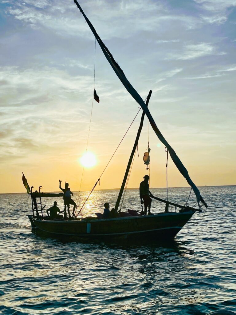 Urtümliches Segelboot mit mehreren Personen auf dem Wasser bei Sonnenuntergang im Gegenlicht