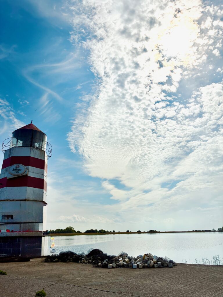 Leuchtturm mit rot-weißen Streifen am Ufer unter bewölktem Himmel