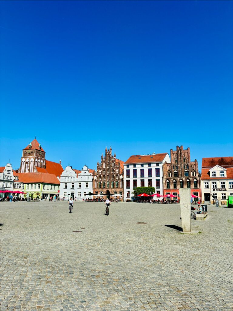 Großer gepflasterter Marktplatz mit historischen Giebelhäusern und blauem Himmel