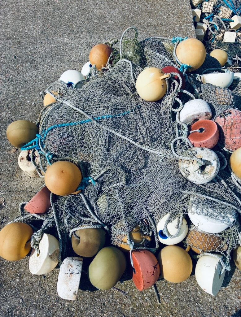 Gefaltetes Fischernetz mit zahlreichen runden Schwimmkörpern in verschiedenen Farben auf einem Betonboden