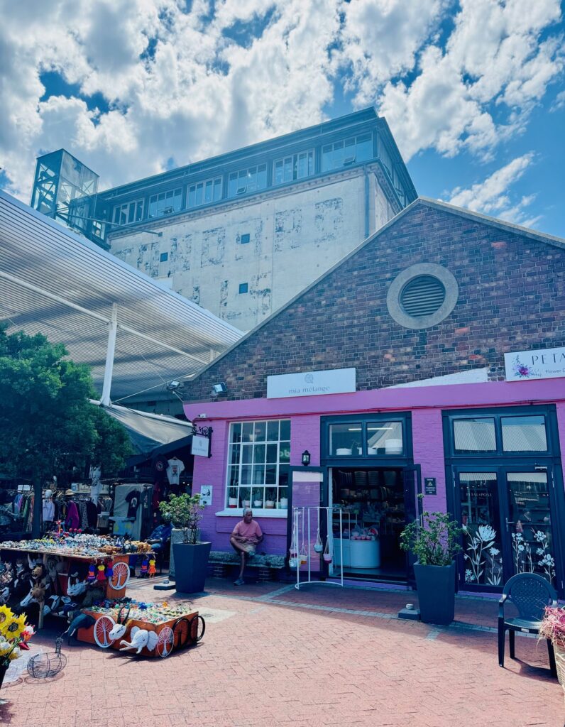 Marktstände mit Kunsthandwerk vor einem rosa gestrichenen Backsteingebäude und einem großen, alten Fabrikgebäude im Hintergrund unter bewölktem Himmel