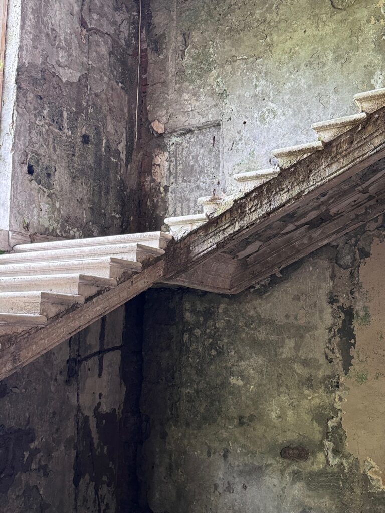 Historische Steintreppe in einem alten, bröckelnden und verwitterten Gebäude mit sichtbaren Rissen und abblätterndem Putz an den Wänden