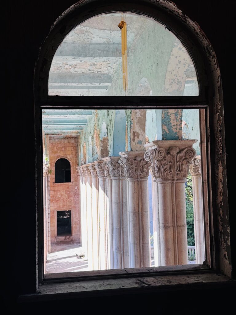 Blick durch ein rundbogiges Fenster auf eine Reihe von verfallenden korinthischen Säulen in einem historischen Gebäude