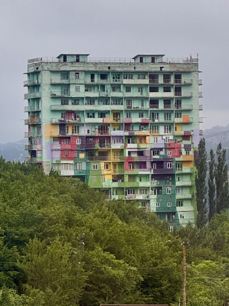 Heruntergekommenes Hochhaus in bunter bemalung mit Balkonen ragt über eine bewaldete Hügelfläche