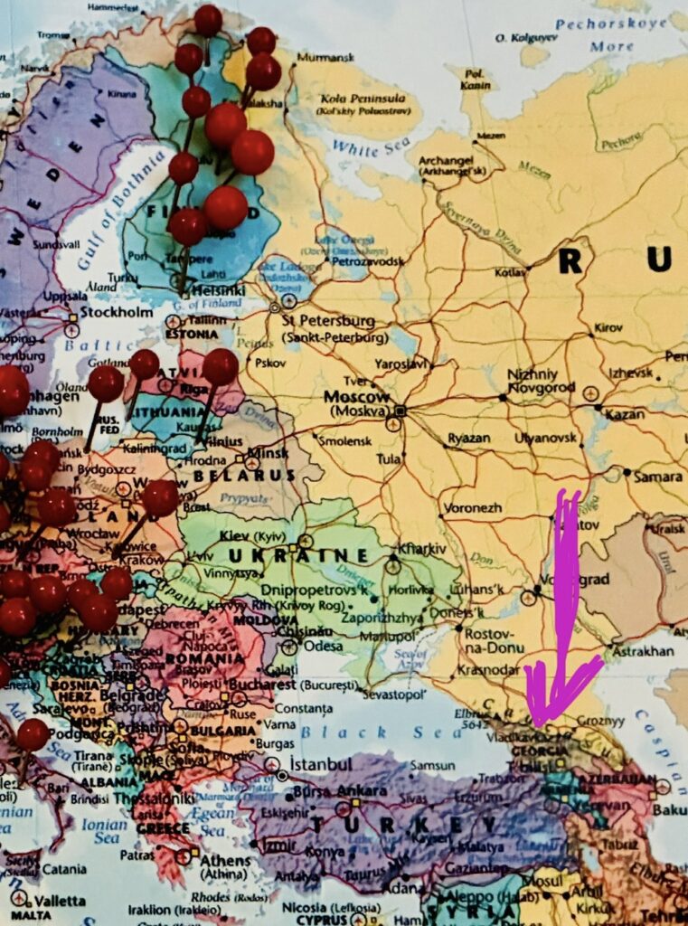 Weltkarte mit vielen Stecknadeln in West-, Zentral- und Nordeuropa und einem Pfeil, der auf Georgien zeigt
