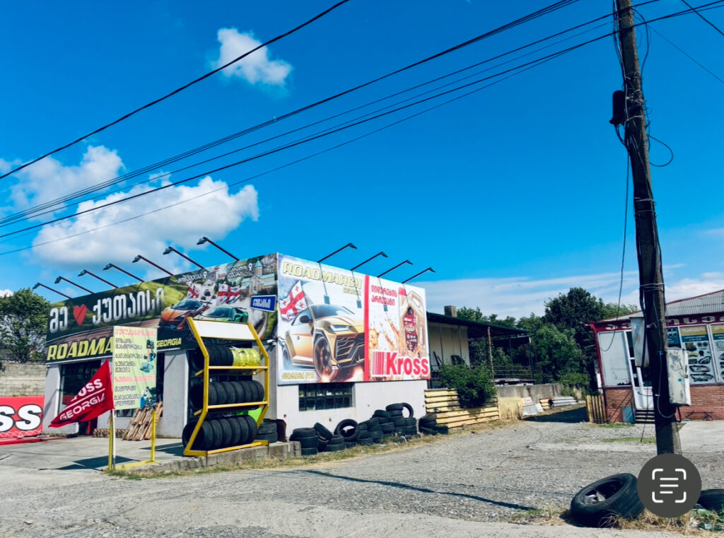 Reifenverkaufsstand mit Reifenstapel und Werbetafeln unter blauem Himmel in Georgien (Kutaisi)