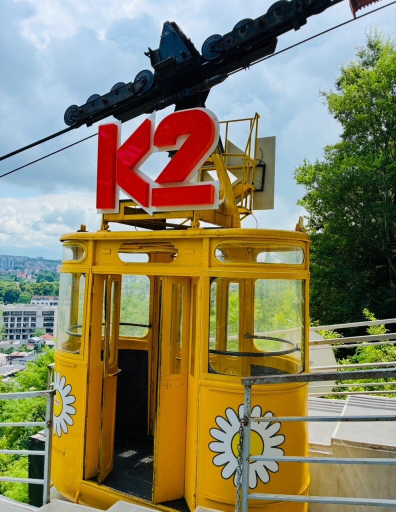 Schmale gelbe Gondel einer Seilbahn mit Blumenmustern und rotem K2-Logo an der Oberseite