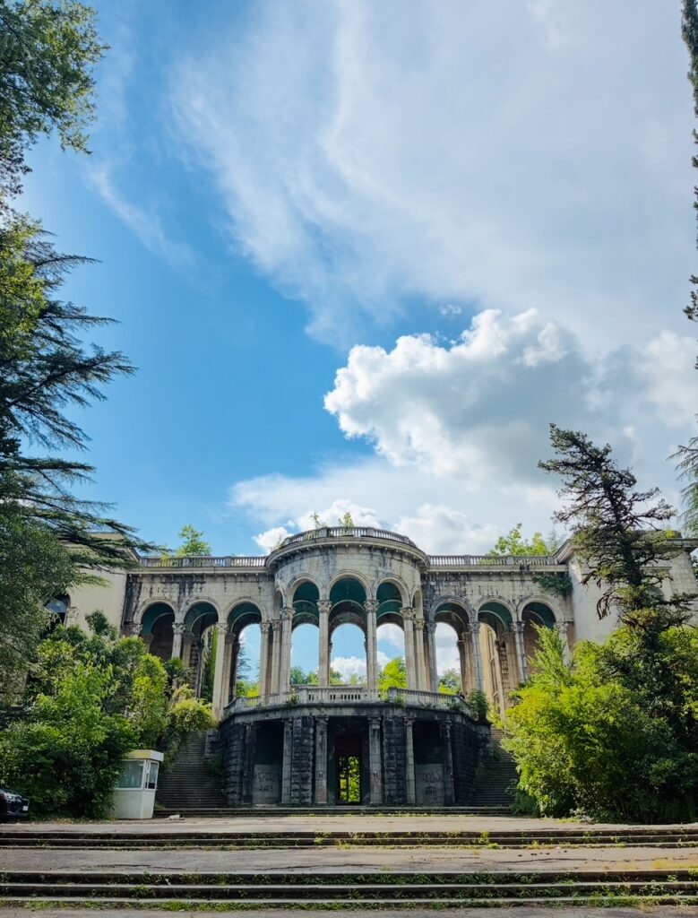 Verfallendes historisches Gebäude mit Säulen und Rundbögen umgeben von Bäumen unter blauem Himmel mit Wolken