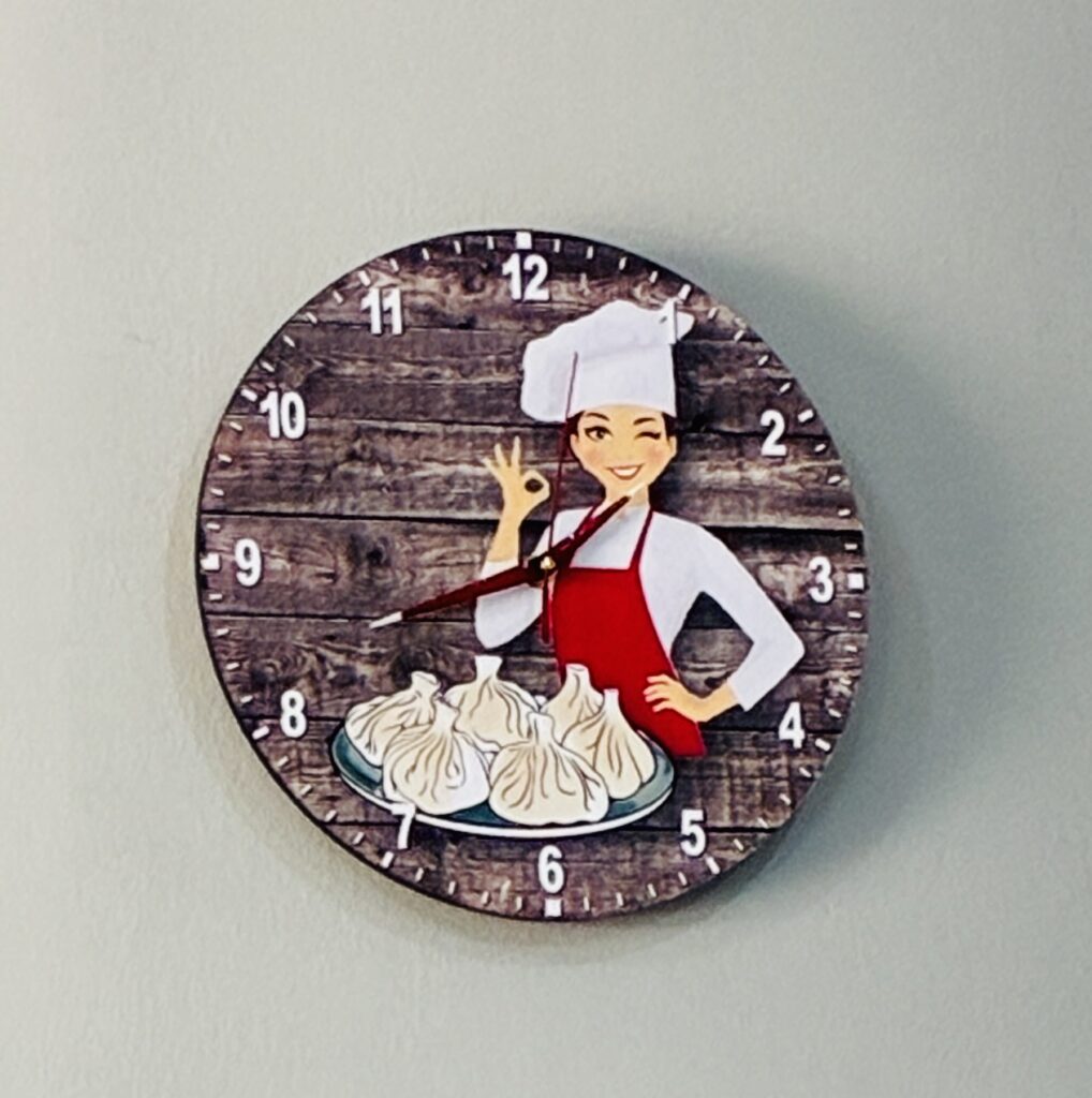 Uhr mit Illustration einer Köchin vor einem Teller mit georgischen Teigtaschen Khinkali