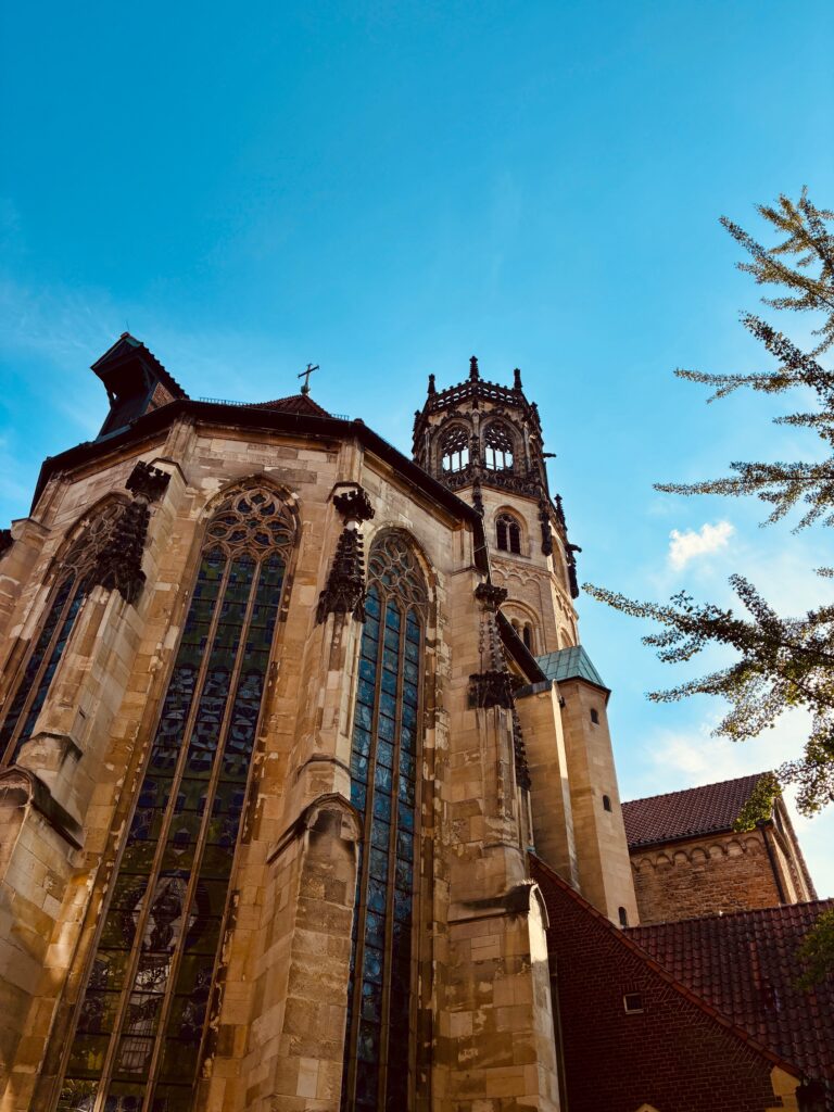 Gotische Kirche mit hohen, spitzbogigen Fenstern und einem Turm vor blauem Himmel