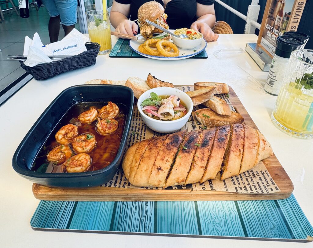 Holzbrett mit getoastetem Brot, einer Schale mit Garnelen in Sauce und einem Schälchen mit Sauce