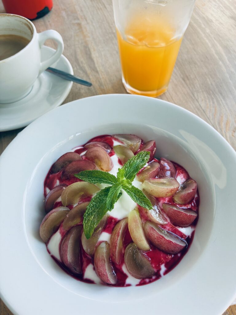 Teller mit Joghurt, dekoriert mit Traubenspalten, daneben ein Glas Orangensaft und eine Tasse mit Kaffee