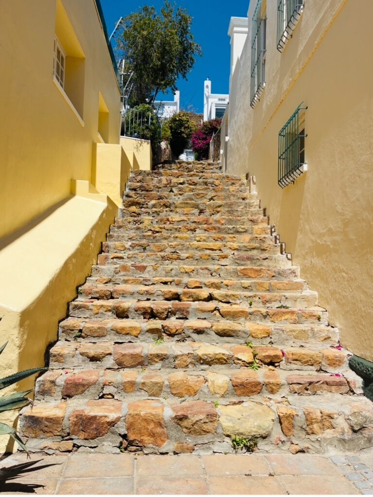 Steintreppe zwischen gelben Häuserwänden unter blauem Himmel