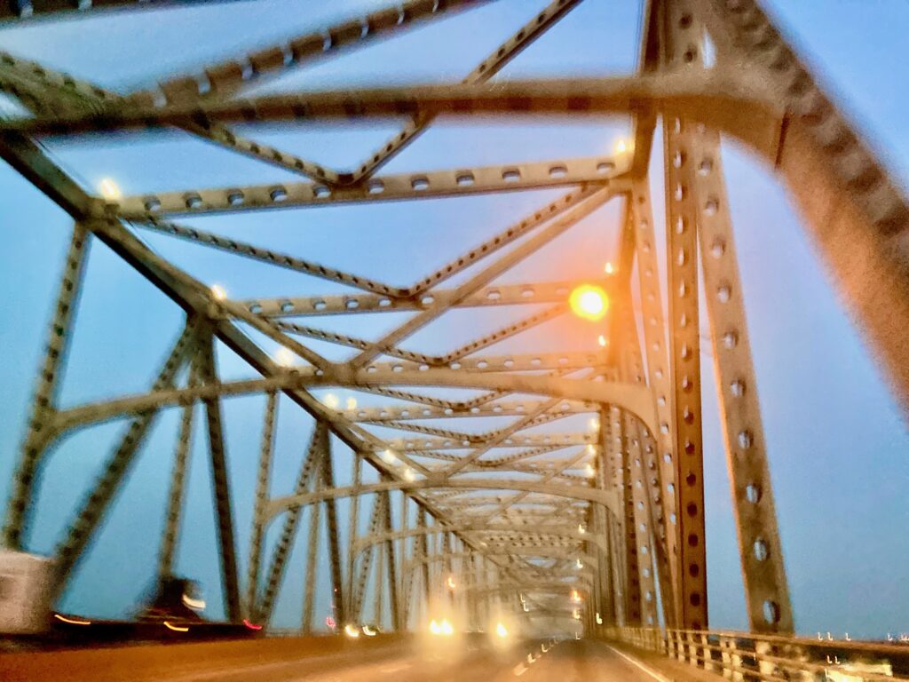 Blick durch das Stahlfachwerk einer beleuchteten Brücke bei Dämmerung