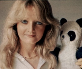 Frau mit blonden, schulterlangen Haaren und weißem Oberteil mit einem Plüschpanda. Die Frau ist die Sängerin Bonnie Tyler