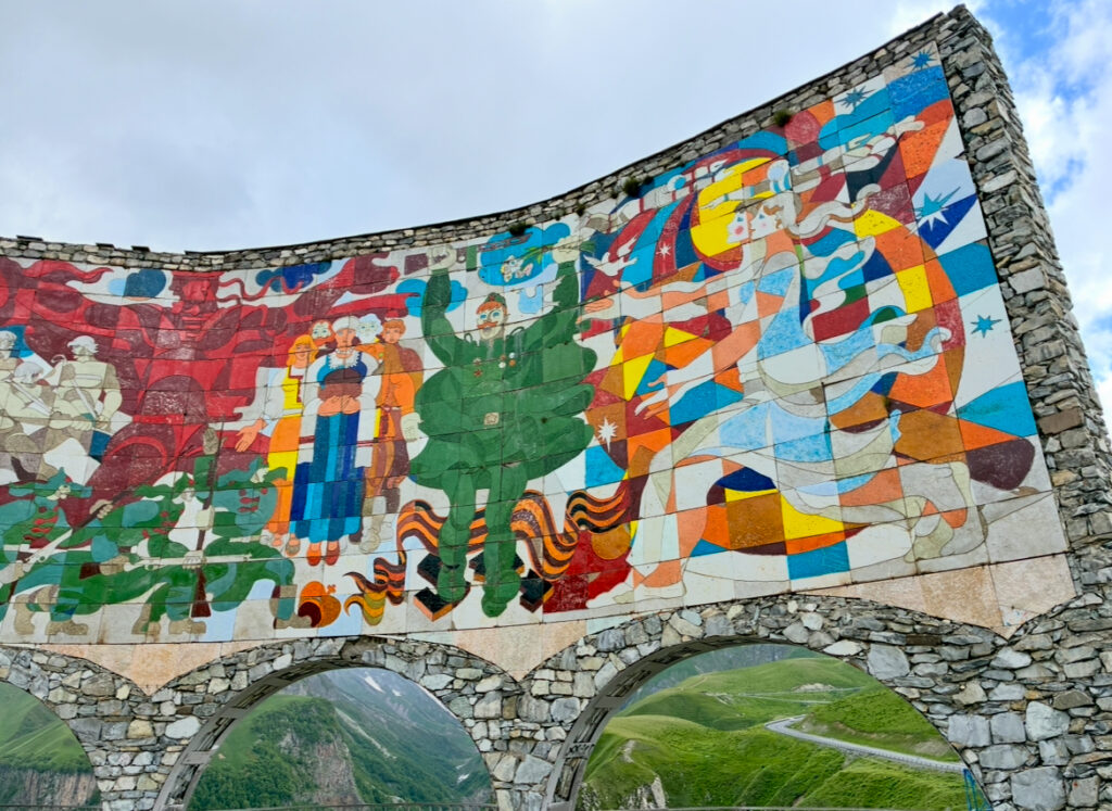 Bunte Mosaikwand mit abstrakten Figuren und Mustern auf einer steinernen Bogen vor Berglandschaft