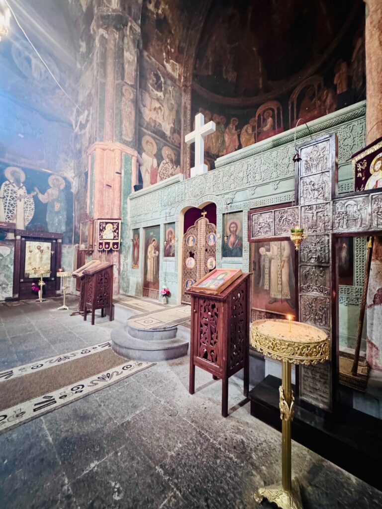 Innenraum einer orthodoxen Kirche mit bemalten Wänden, einem großen weißen Kreuz und mehreren hölzernen Lesepulten