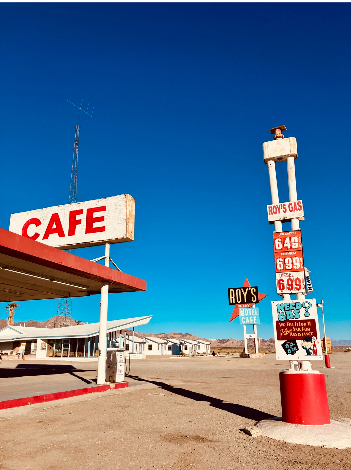 Altmodische Tankstelle und Café mit mehreren Schildern in einer Wüstenlandschaft unter klarem blauem Himmel