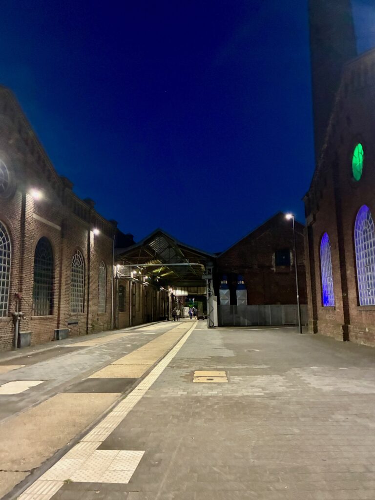 Blick in einen nächtlichen Fabrikhof mit Backsteinbauten und beleuchteten Fenstern