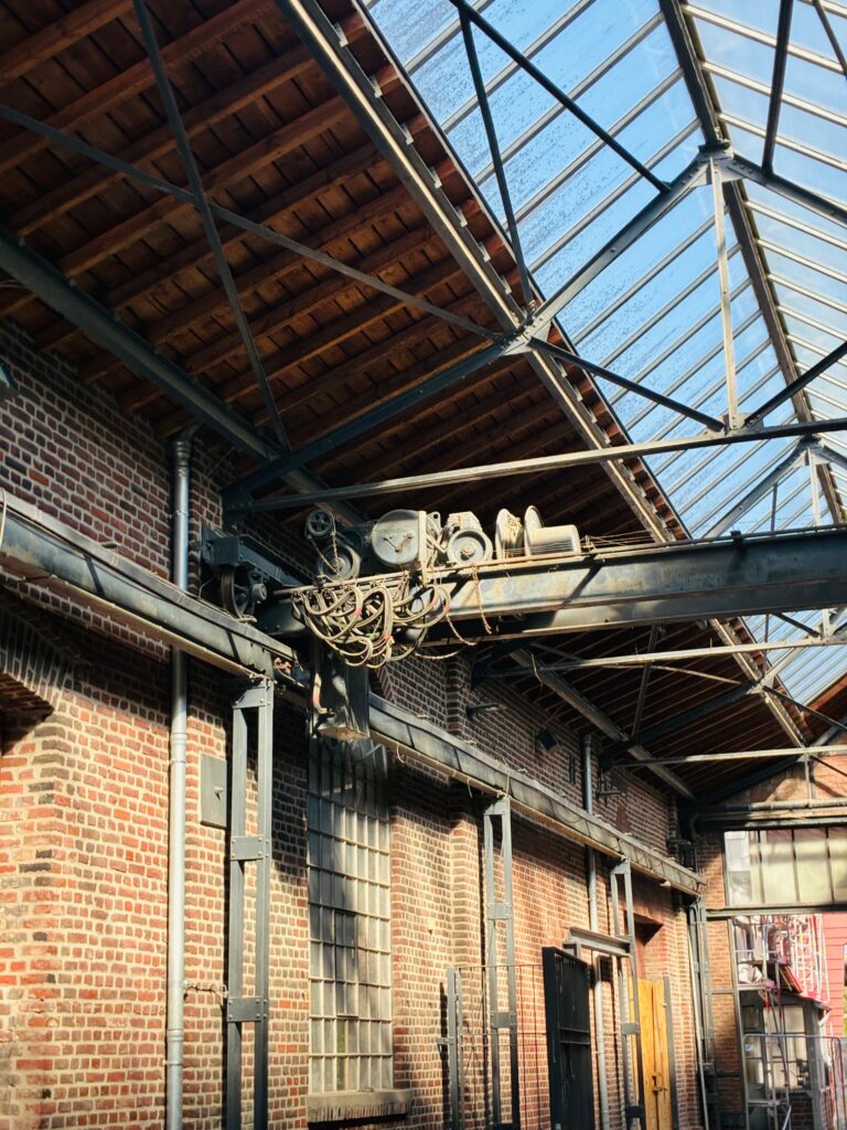 Industrielle Halle mit Backsteinwänden, großen Fenstern und einem Kranlaufwerk unter einem Glasdach