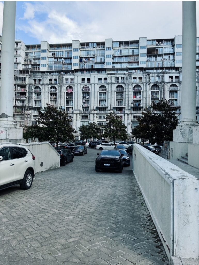 Blick auf einen gepflasterten Innenhof mit geparkten Autos und einem mehrstöckigen Wohngebäude im Hintergrund