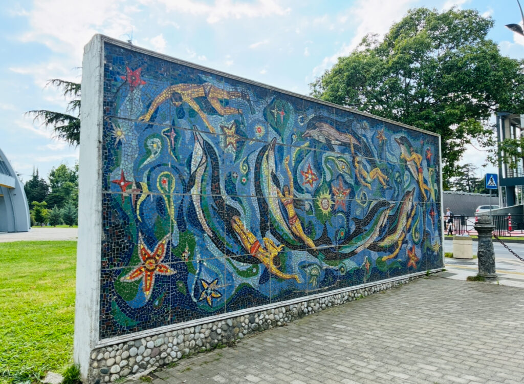 Großes Mosaik mit stilisierten Meeresbewohnern und Schwimmern an einer Außenwand in einem Park