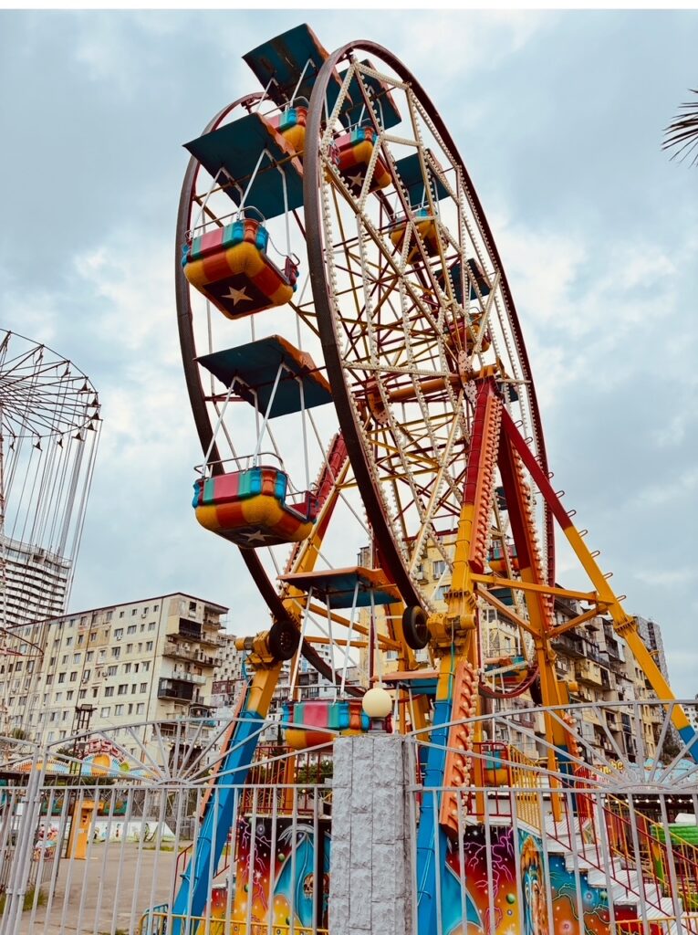 Buntes Riesenrad mit überdachten Gondeln vor mehrstöckigen Wohngebäuden unter bewölktem Himmel