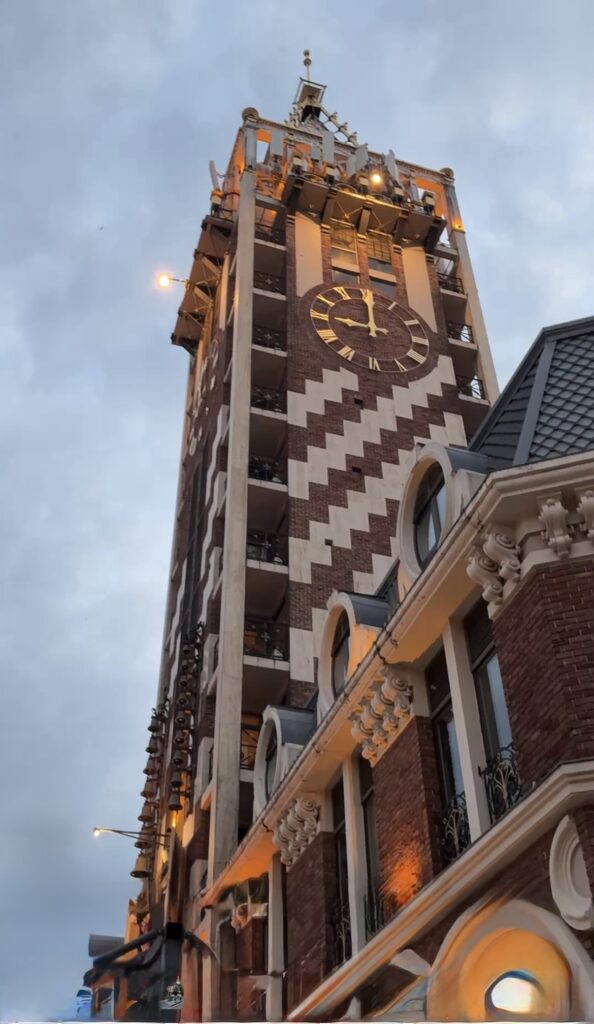Uhrenturm mit Zifferblatt und Ziegelmuster vor bewölktem Himmel in der Dämmerung