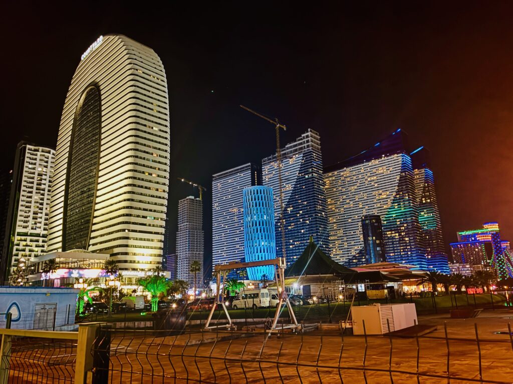 Nächtliche Stadtansicht von Orbi City in Batumi, Georgien, mit modernen, beleuchteten Hochhäusern und Baukränen im Vordergrund