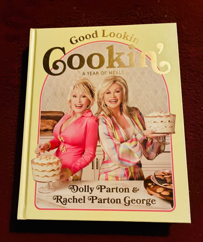 Buchcover mit zwei lächelnden Frauen, eine hält eine Torte, die andere ein Dessert, Titel in Golddruck: 'Good Lookin' Cookin' A Year of Meals', Autoren 'Dolly Parton & Rachel Parton George'