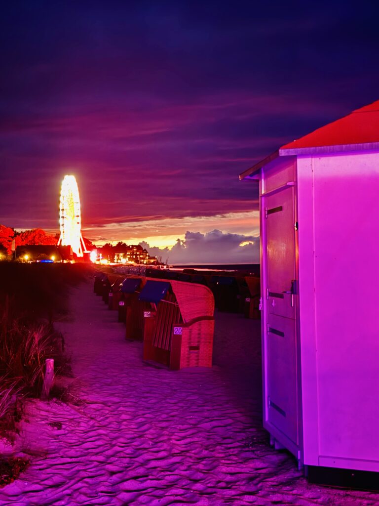 Strandweg mit Strandkörben und beleuchtetem Riesenrad bei Sonnenuntergang