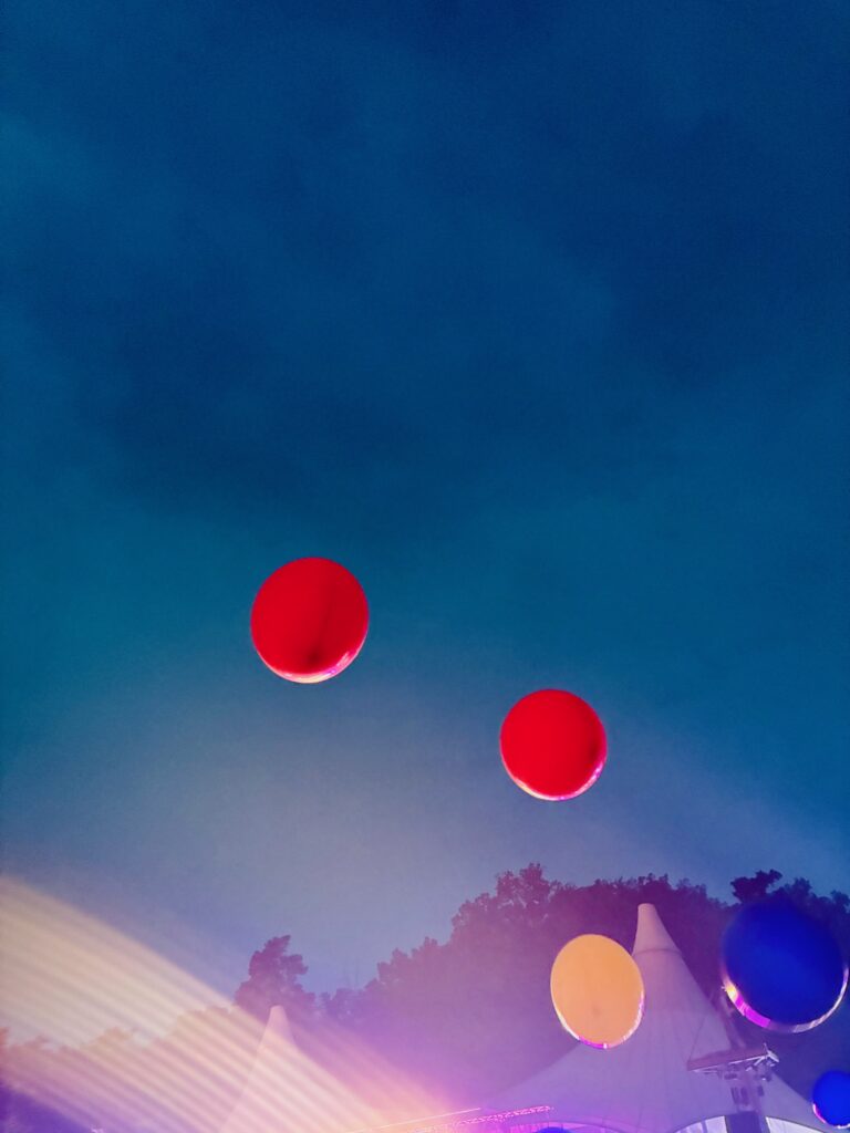 Mehrere große Luftballons vor einem Abendhhimmel über Bäumen