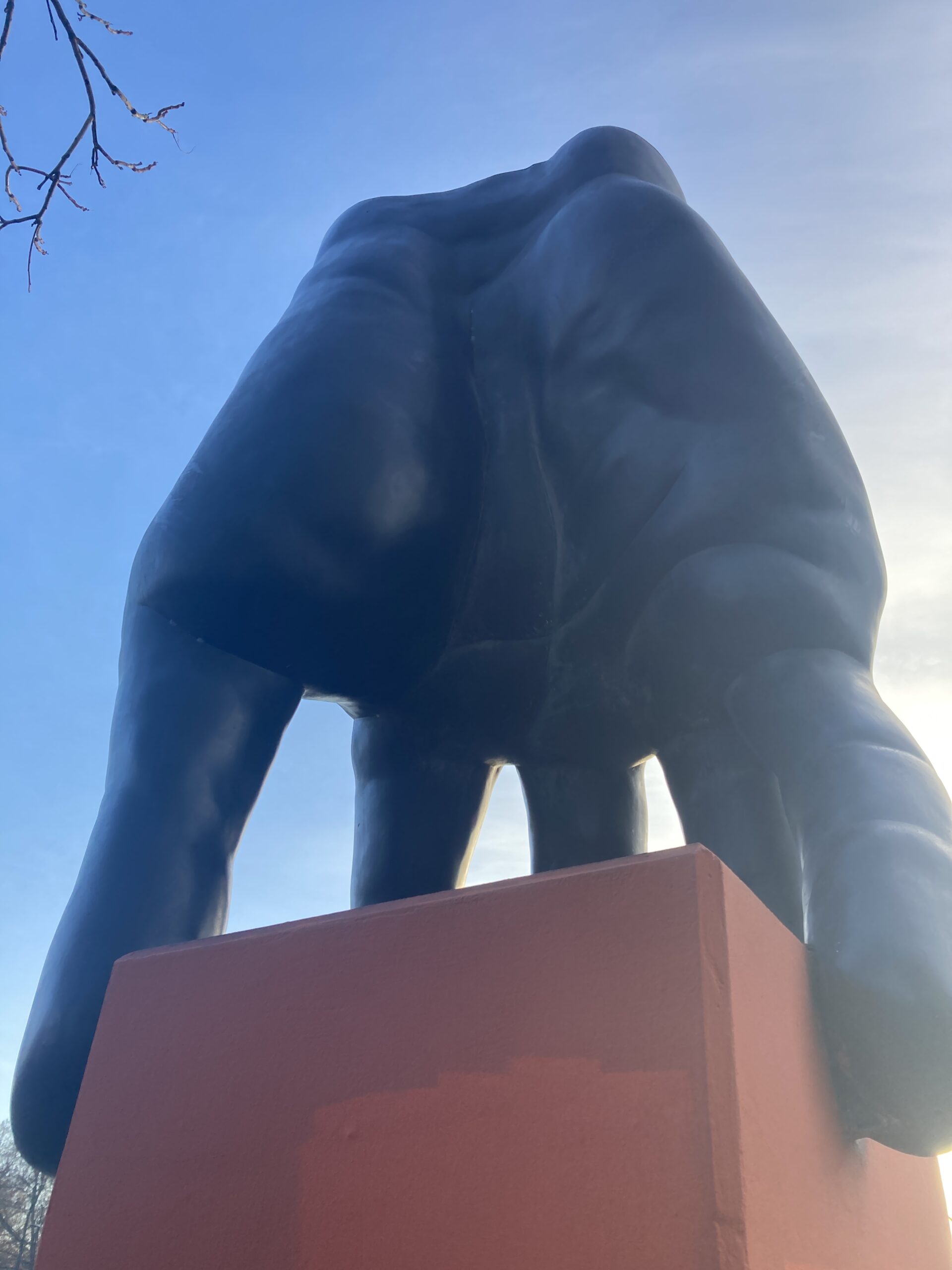 Nahaufnahme einer großen schwarzen Handskulptur auf einem roten Sockel vor blauem Himmel