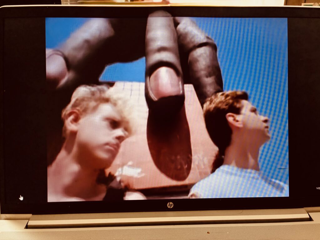 Laptopbildschirm zeigt zwei junge Männer vor einer großen Hand-Skulptur vor blauem Himmel. Die beiden Männer sind Martin Gore und Dave Gahan von der Band Depeche Mode