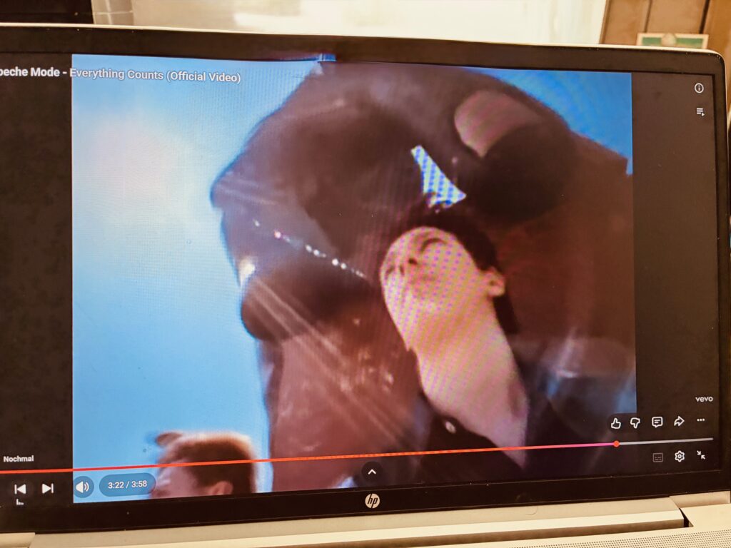 Laptopbildschirm zeigt ein Musikvideo mit einer Person, die den Kopf nach hinten neigt, über ihr die riesige Skulptur einer Hand.